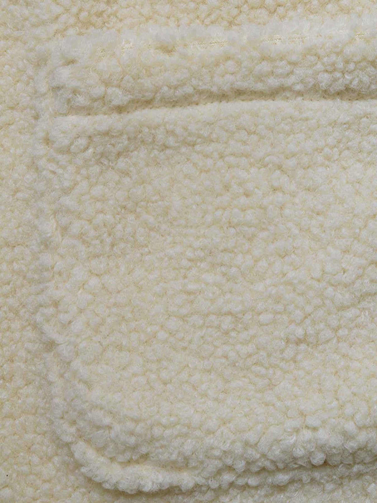Close-up of a cream-colored sherpa fleece fabric with a soft, textured loop pile and a stitched pocket edge.