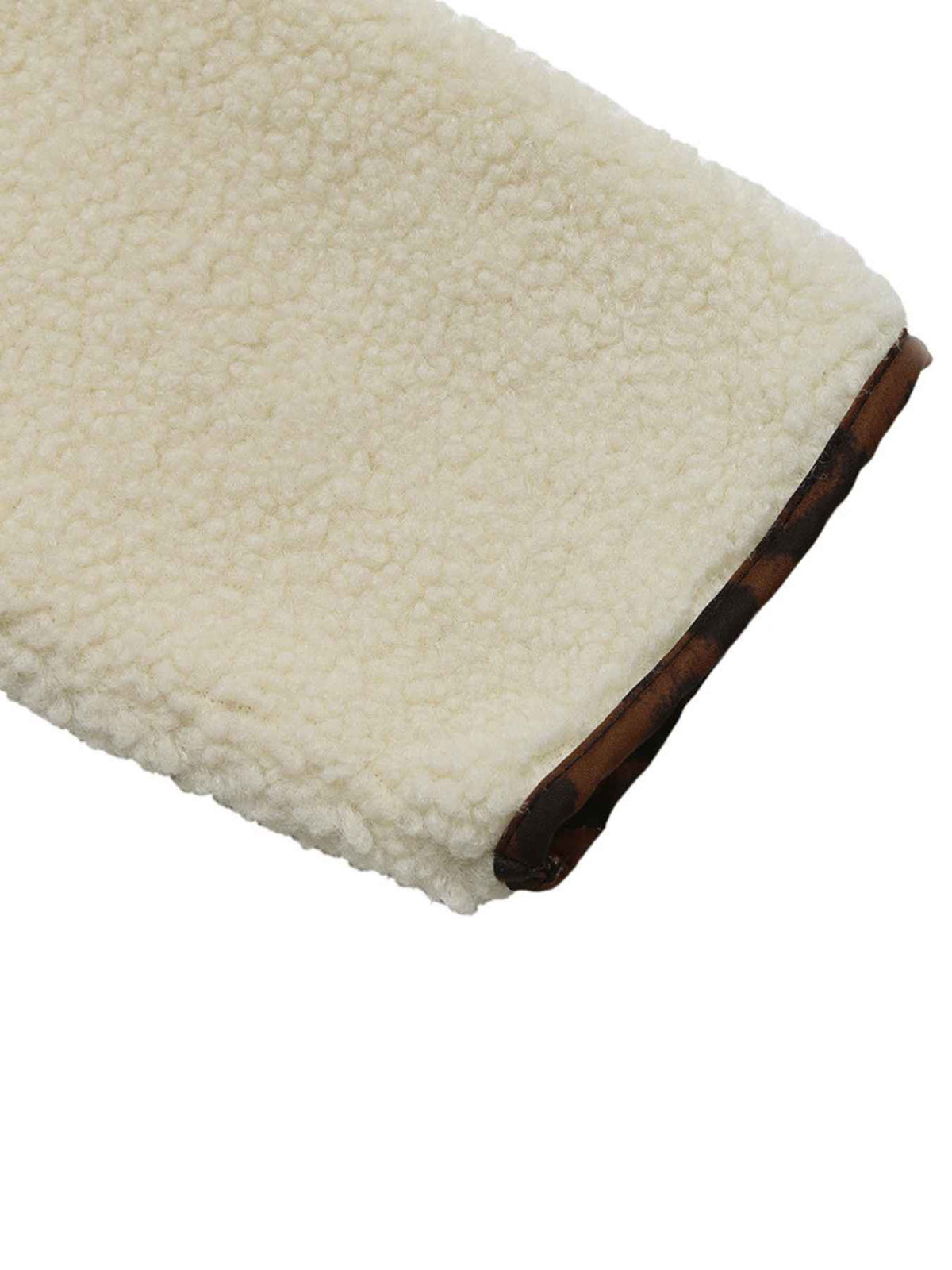 Close-up of a cream sherpa fleece fabric with a dark brown trim along the edge, shown on a plain white background.