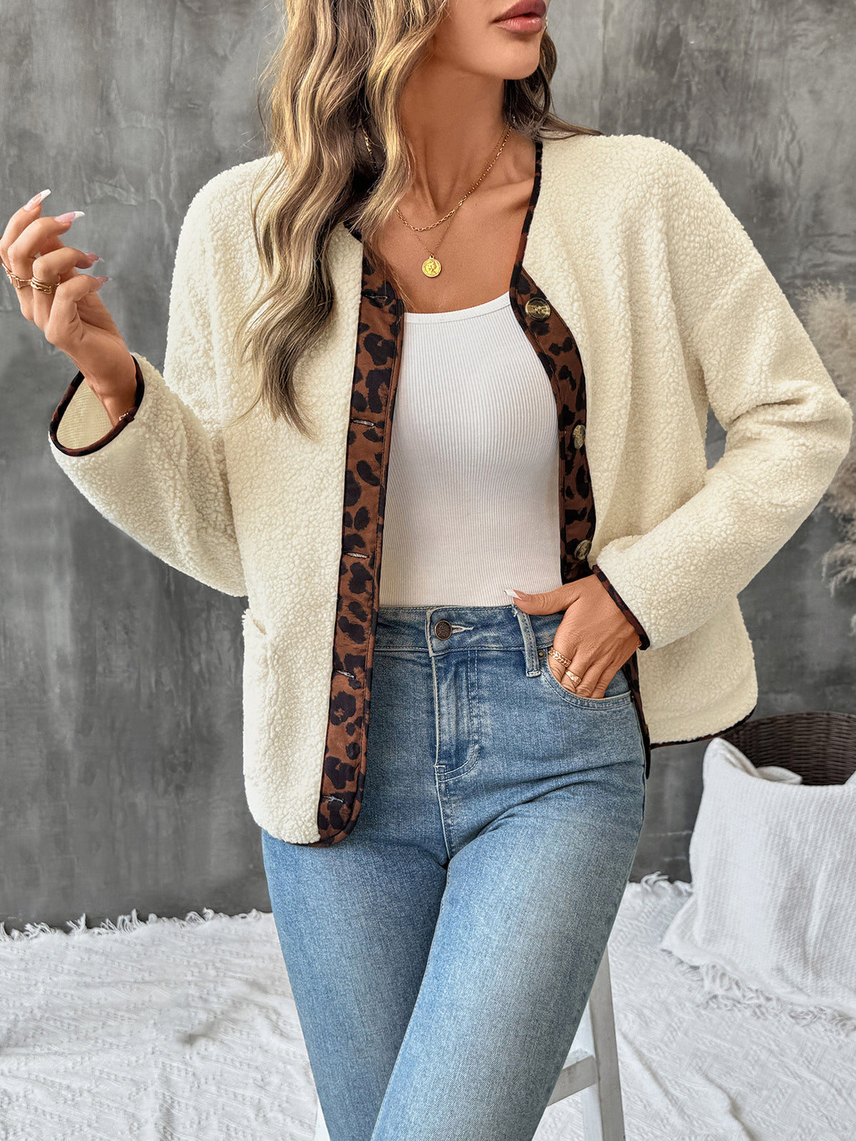 Woman wearing a cream cardigan with leopard print trim, white top, and blue jeans against a gray wall.