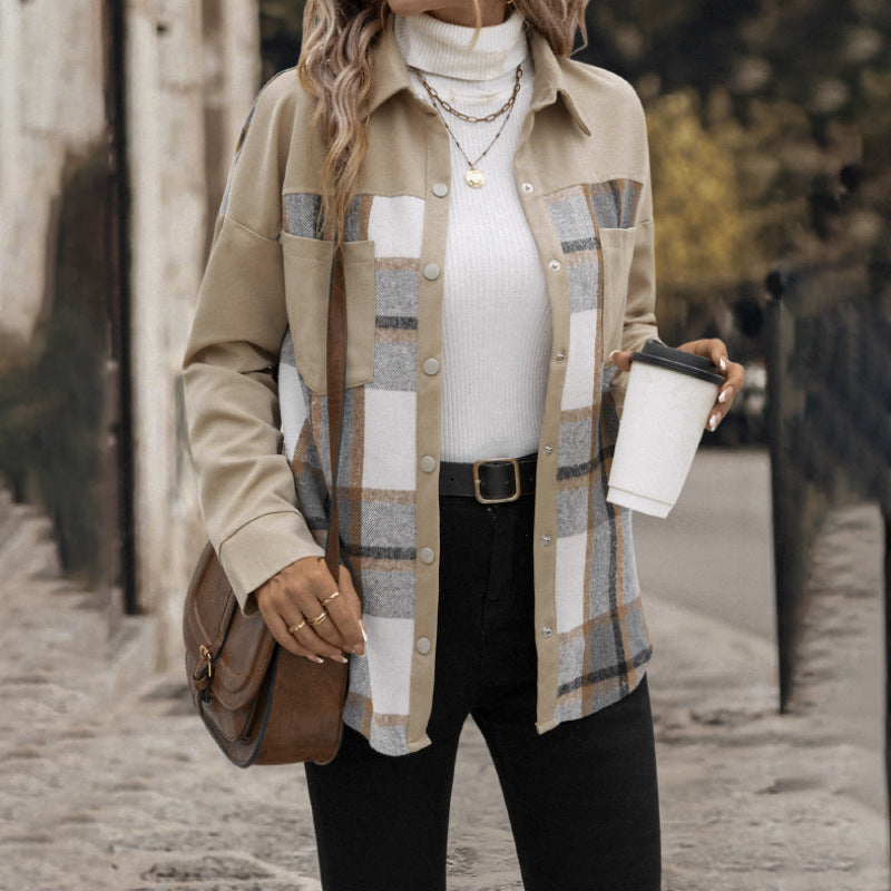 A woman wearing a beige button-up shirt jacket with a plaid pattern in beige, gray, and white over a white ribbed turtleneck, paired with black pants and carrying a brown leather shoulder bag while holding a coffee cup.