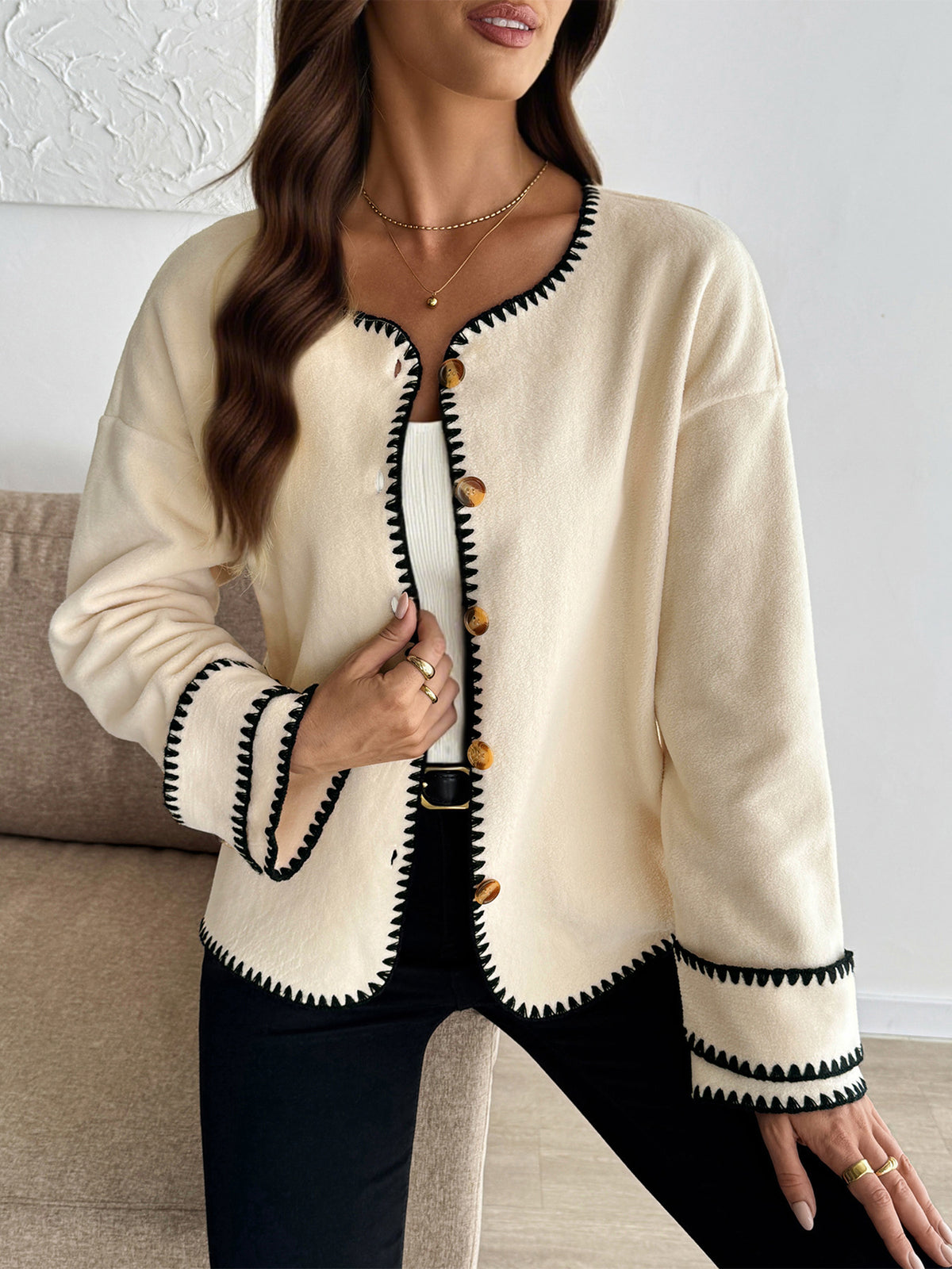 Woman wearing a cream cardigan with black trim in a living room setting