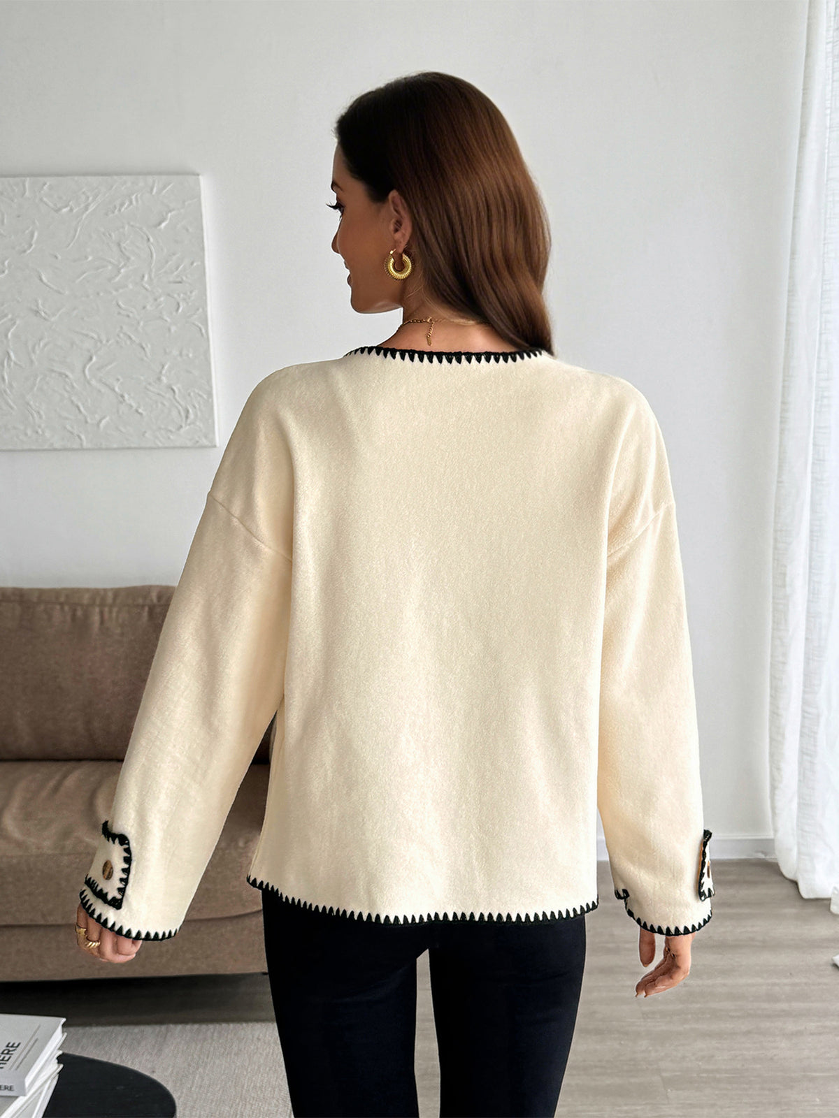 Woman wearing a cream sweater with black trim in a room.