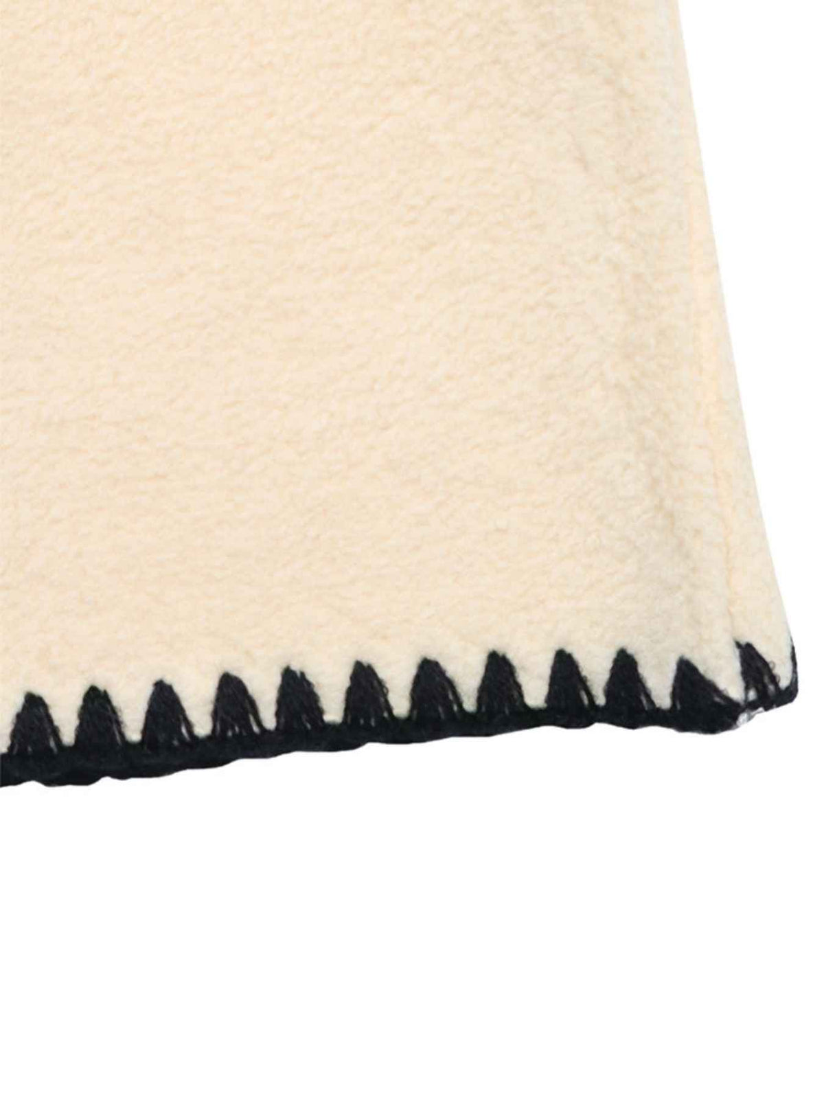 Close-up of a cream-colored plush or fleece fabric with a black zigzag stitched border on a white background.
