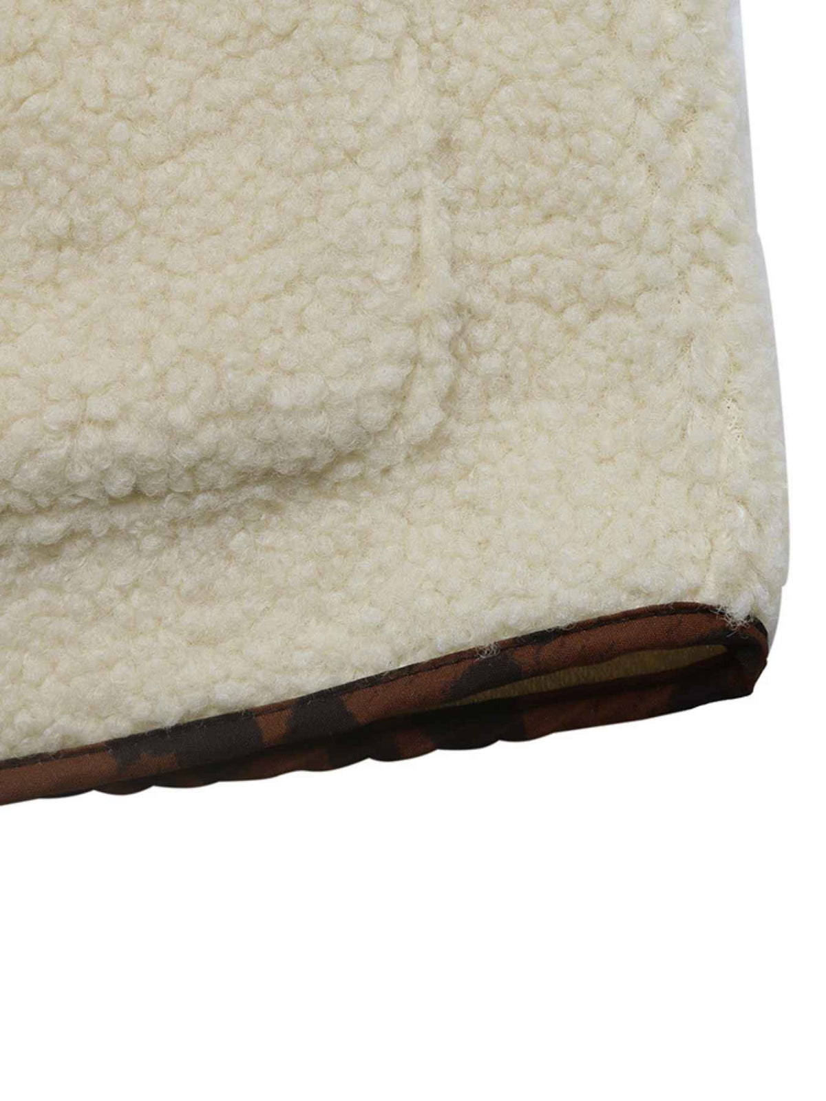 Close-up of a cream sherpa fleece fabric corner showing a brown patterned trim along the edge, isolated on a white background.