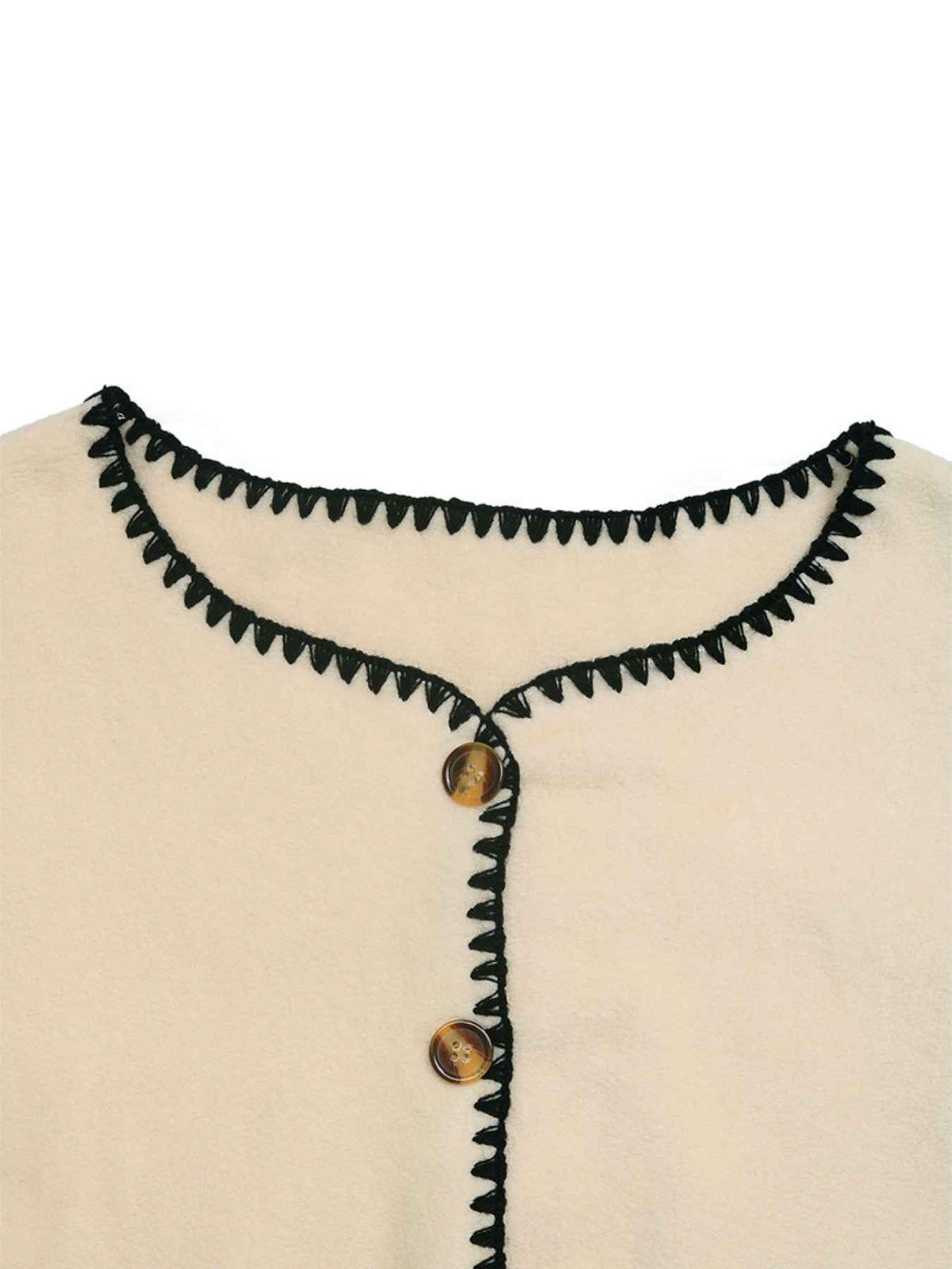 Close-up of a cream-colored top with black zigzag trim around the neckline and down the front placket, featuring two brown buttons.