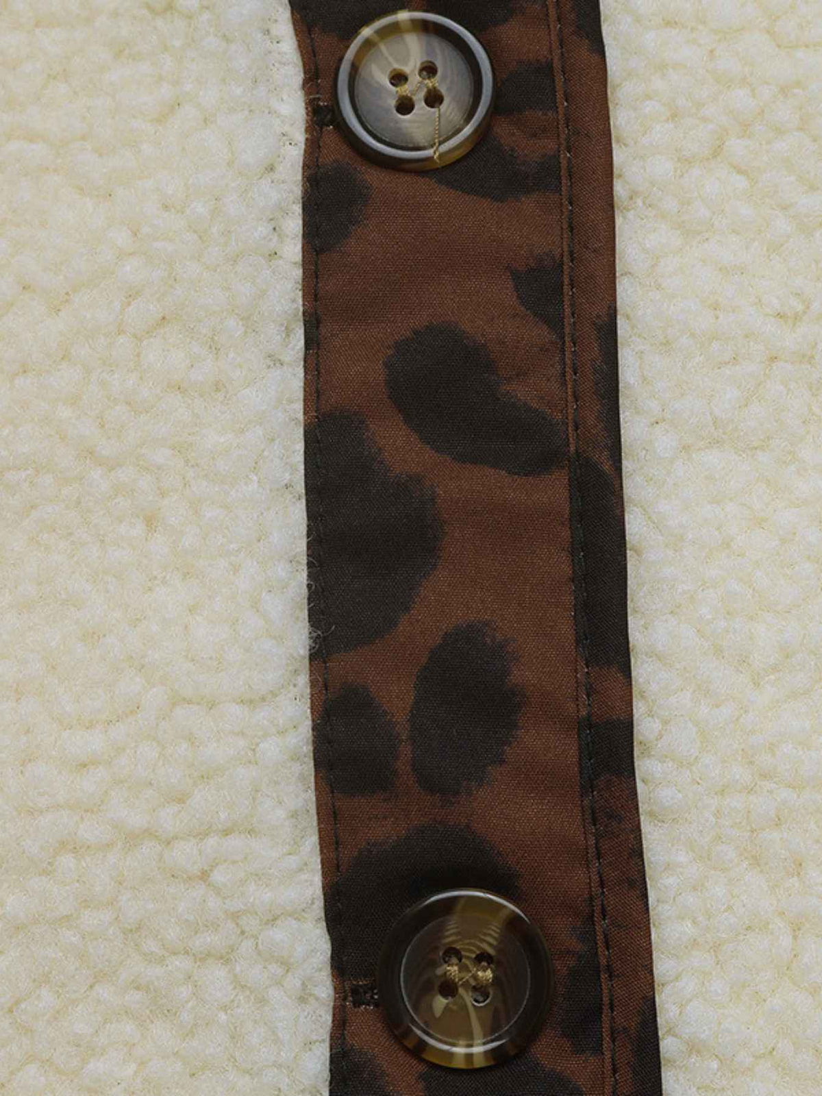 Close-up of a garment detail showing a cream sherpa fleece body, a vertical brown leopard-print placket, and two decorative buttons.