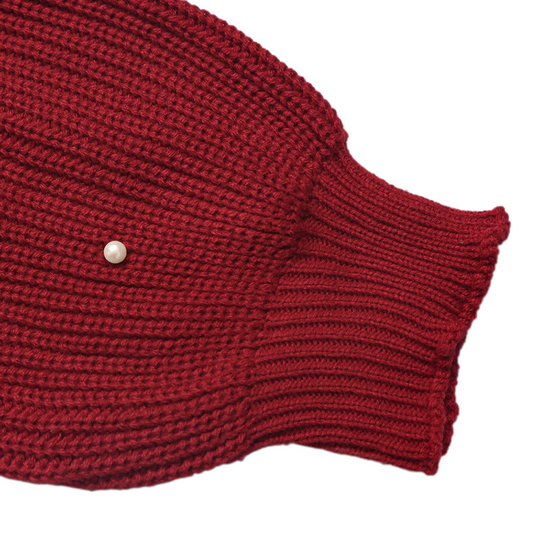 Close-up of a dark red ribbed knit garment, showing the texture of the knit fabric and a small light-colored button on the sleeve cuff, set against a plain white background.