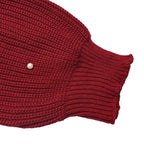 Close-up of a dark red ribbed knit garment, showing the texture of the knit fabric and a small light-colored button on the sleeve cuff, set against a plain white background.