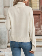 Person wearing a beige sweater and blue jeans standing outdoors.