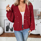Person wearing a red knitted cardigan with white buttons in a room setting.