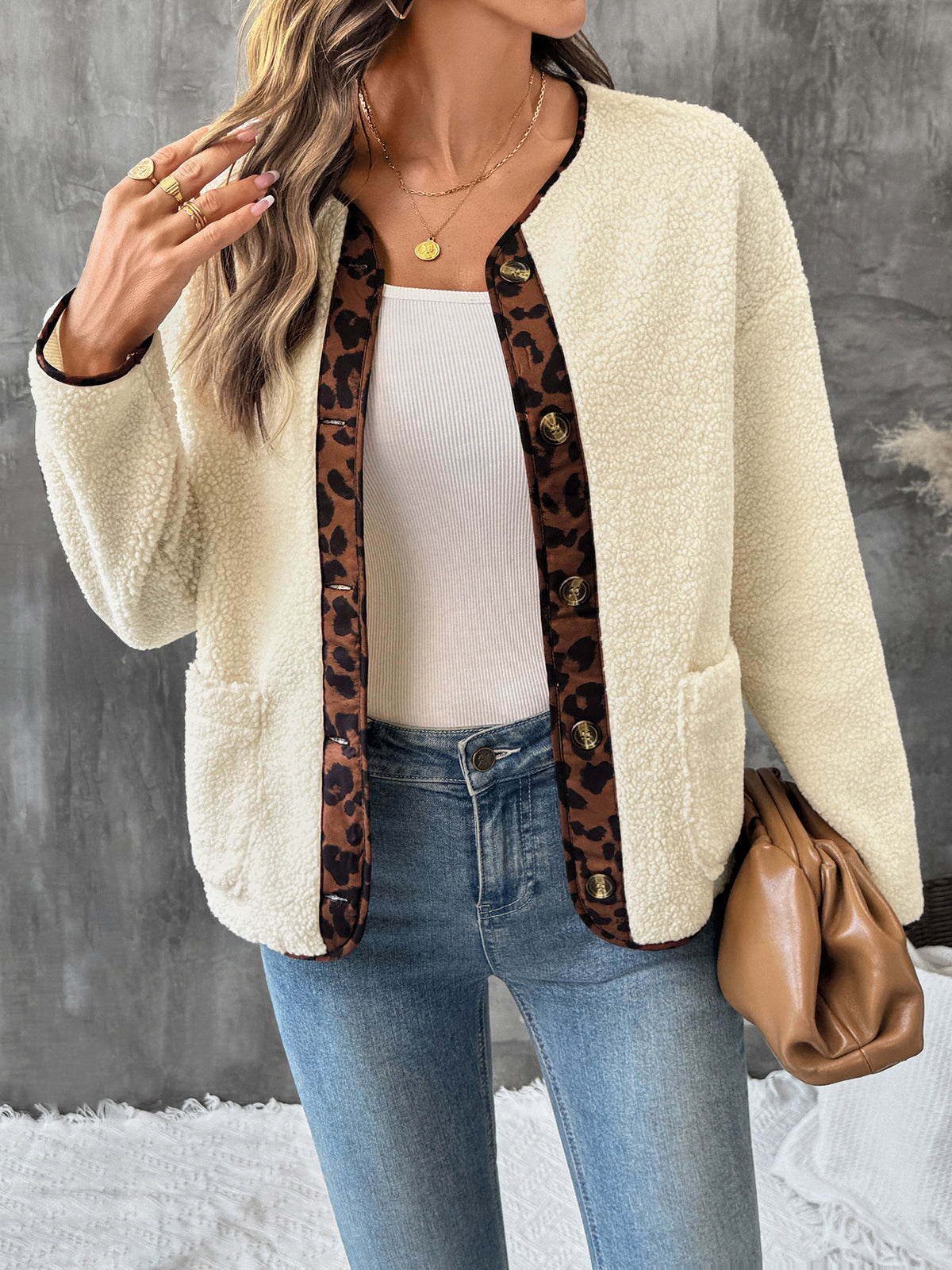 Woman wearing a cream cardigan with leopard print trim, white top, blue jeans, and brown bag against a gray background.