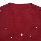 Close-up of a red ribbed knit cardigan sweater with a V-neck, decorative pearl-like buttons, and a central silver floral embellishment.
