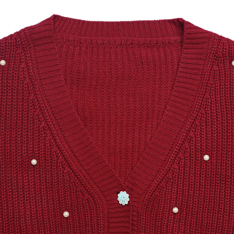 Close-up of a red ribbed knit cardigan sweater with a V-neck, decorative pearl-like buttons, and a central silver floral embellishment.