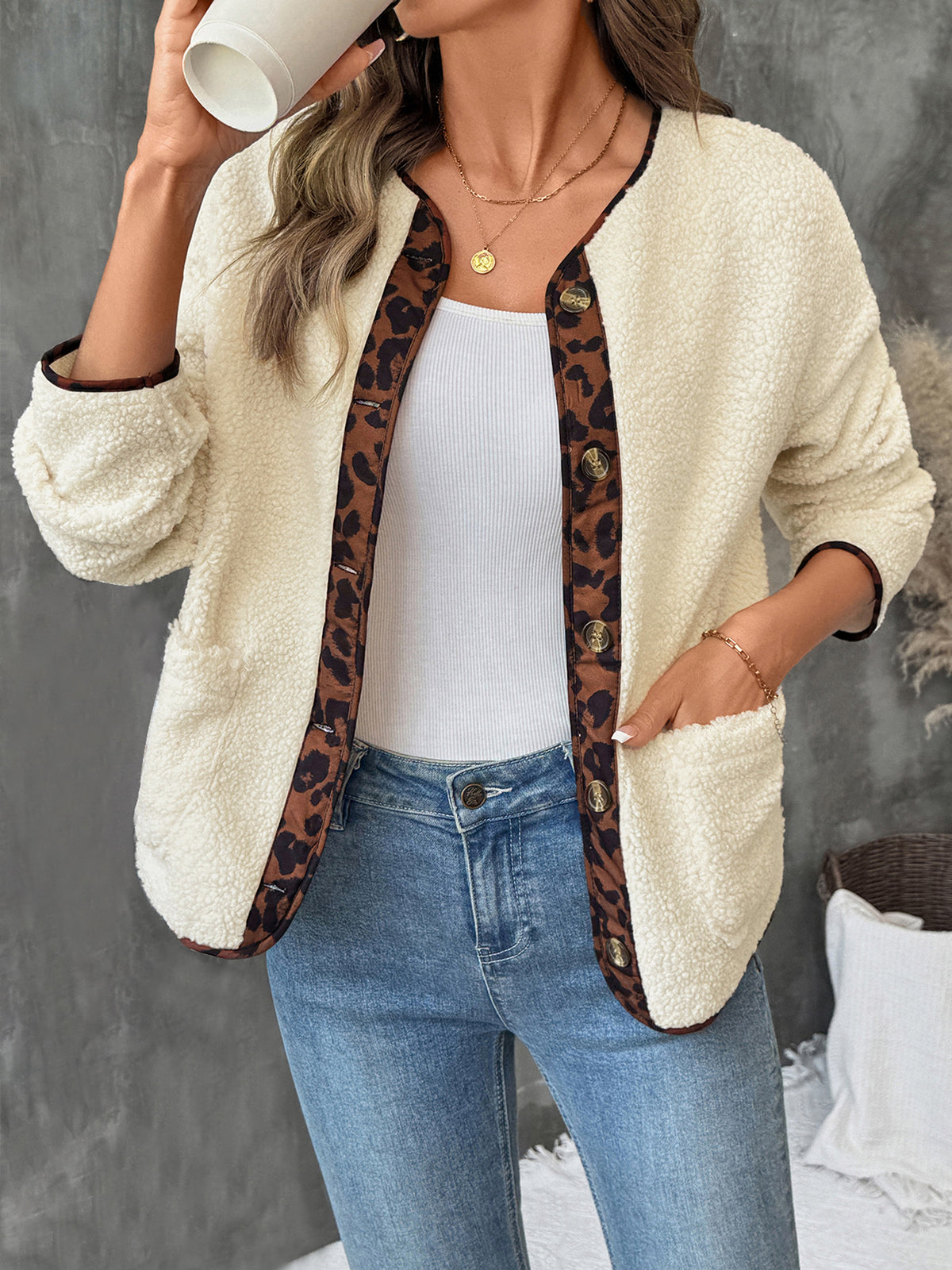 Woman wearing a cream cardigan with leopard print trim, white top, and blue jeans.