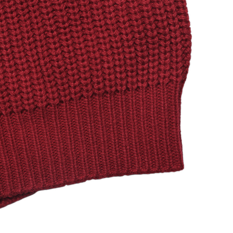 Close-up detail of a chunky knit garment in a deep burgundy red, showing the ribbed cuff against a plain white background.