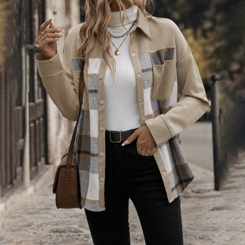 A woman wearing a beige button-front overshirt with a large plaid pattern panel in beige, gray, white, and brown, layered over a white ribbed turtleneck and black pants, standing on a cobblestone street.