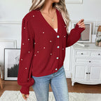 Person wearing a red knitted cardigan with pearl buttons in a room.
