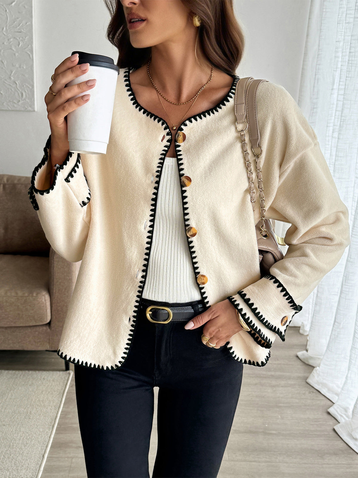 Woman wearing a beige cardigan with black trim, holding a white cup.