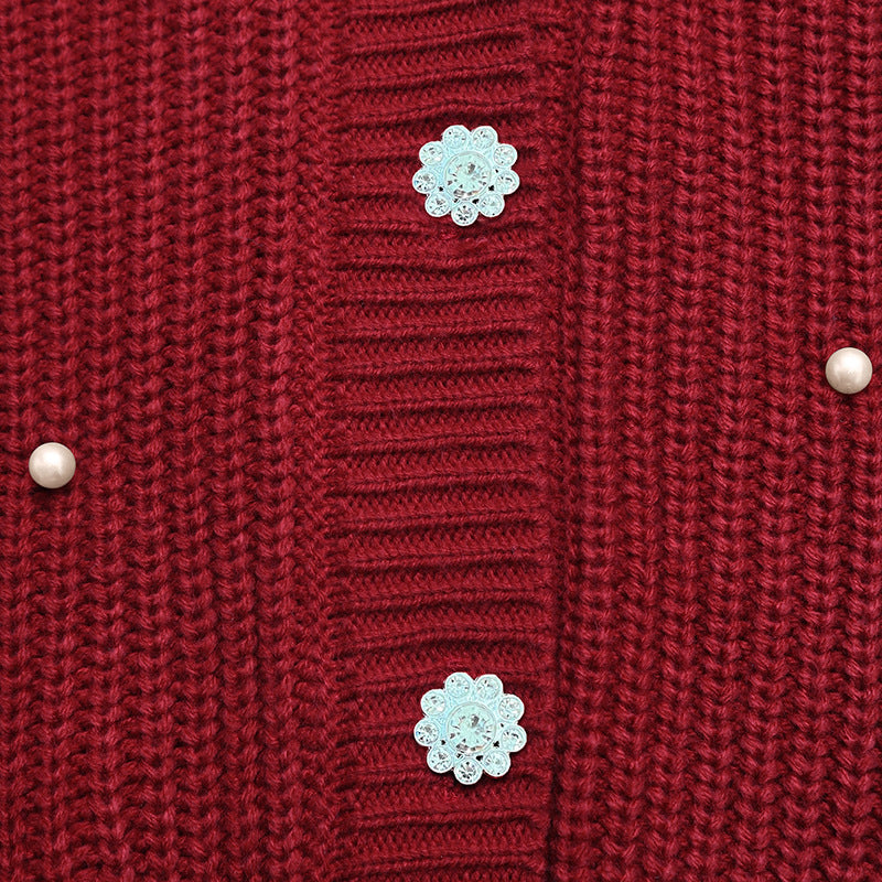 Close-up of a red knit cardigan sweater showing the ribbed front panel, decorative light blue flower-shaped buttons, and small pearl-like buttons on the sides.