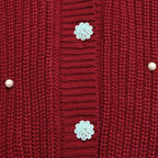 Close-up of a red knit cardigan sweater showing the ribbed front panel, decorative light blue flower-shaped buttons, and small pearl-like buttons on the sides.