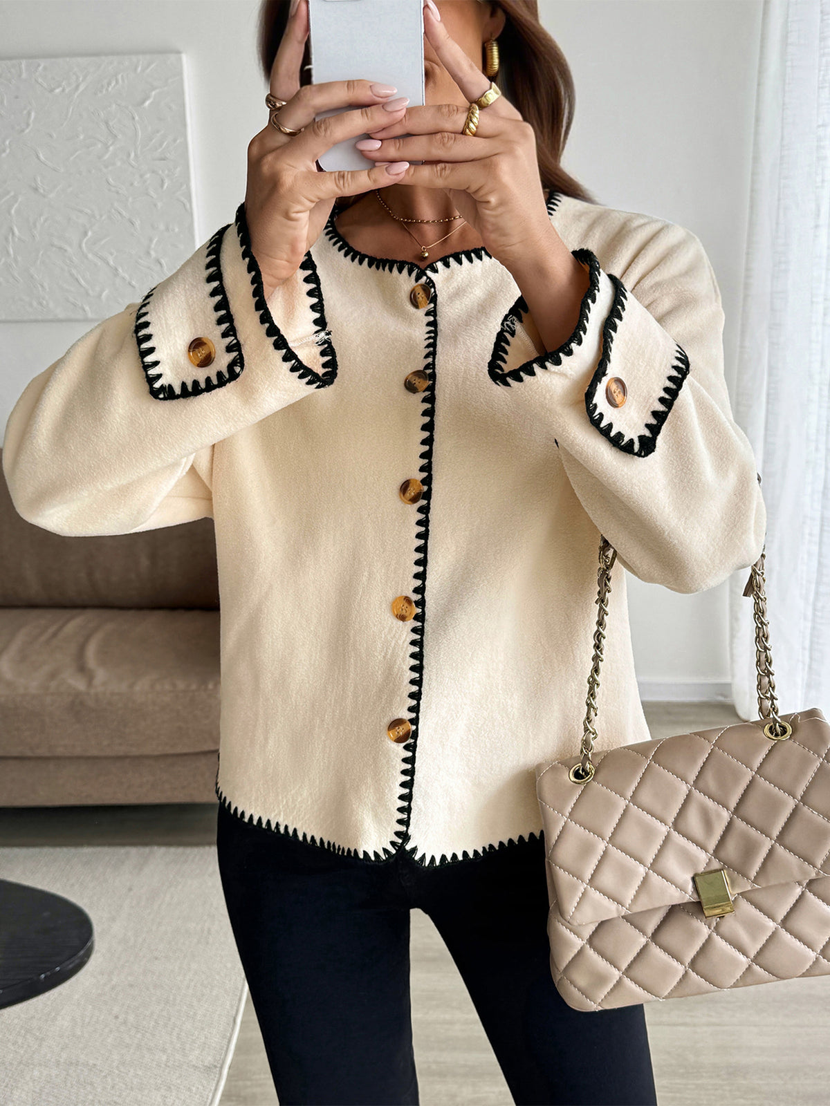 Person wearing a cream jacket with black trim and holding a beige handbag.