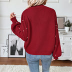 Person wearing a red sweater with pearl embellishments in a home setting.