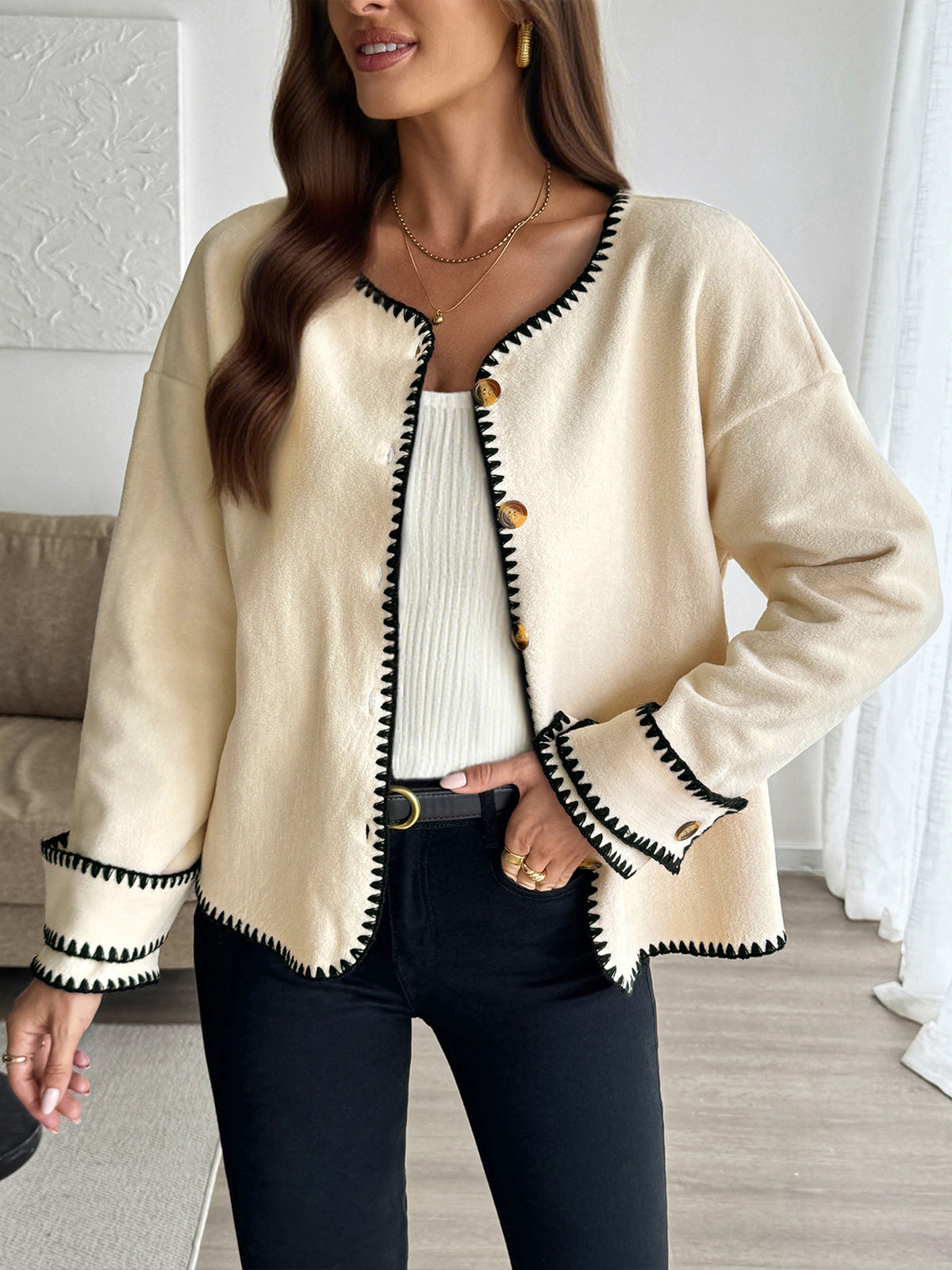 Woman wearing a beige cardigan with black trim in an indoor setting