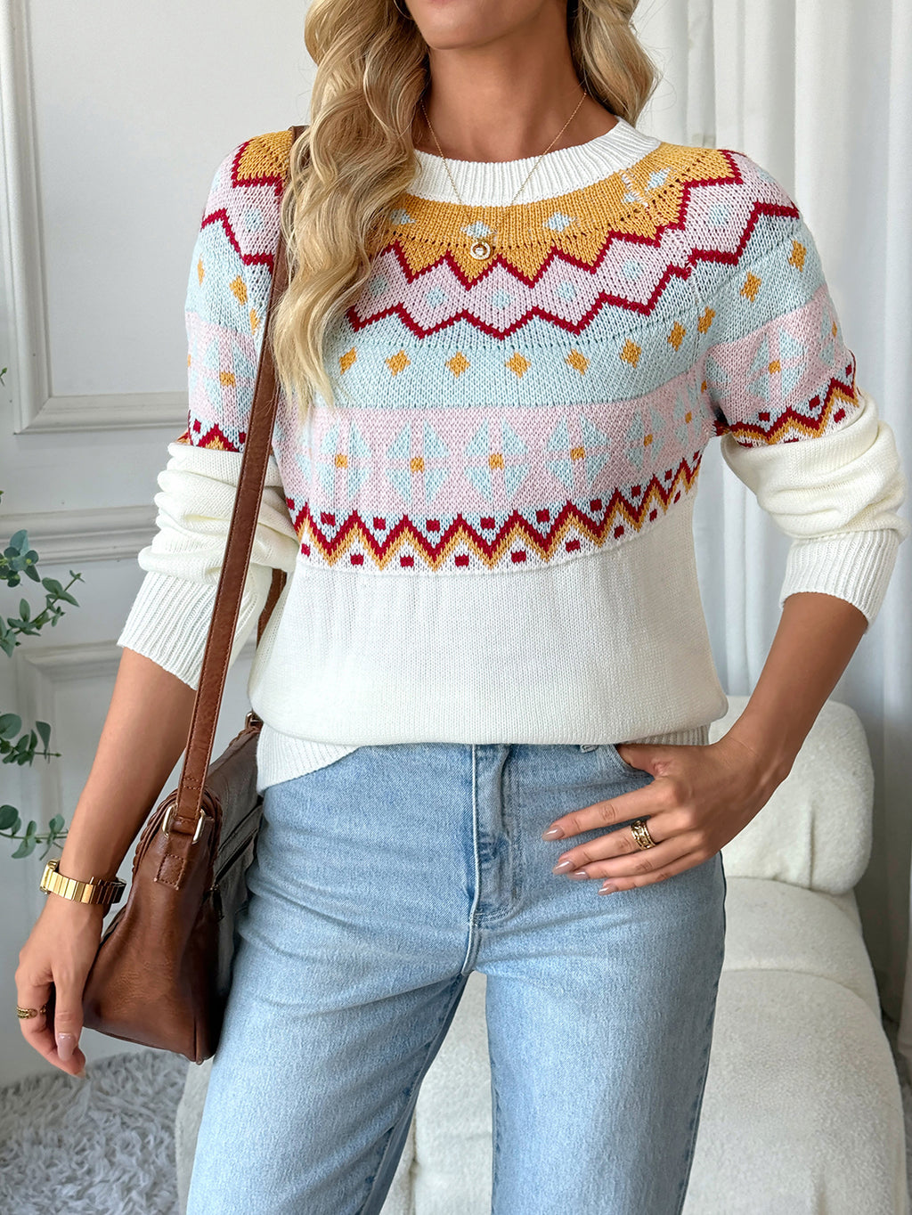 Woman wearing a colorful patterned sweater and light blue jeans indoors.