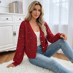 Woman wearing a red cardigan with pearl embellishments sitting on a white rug.