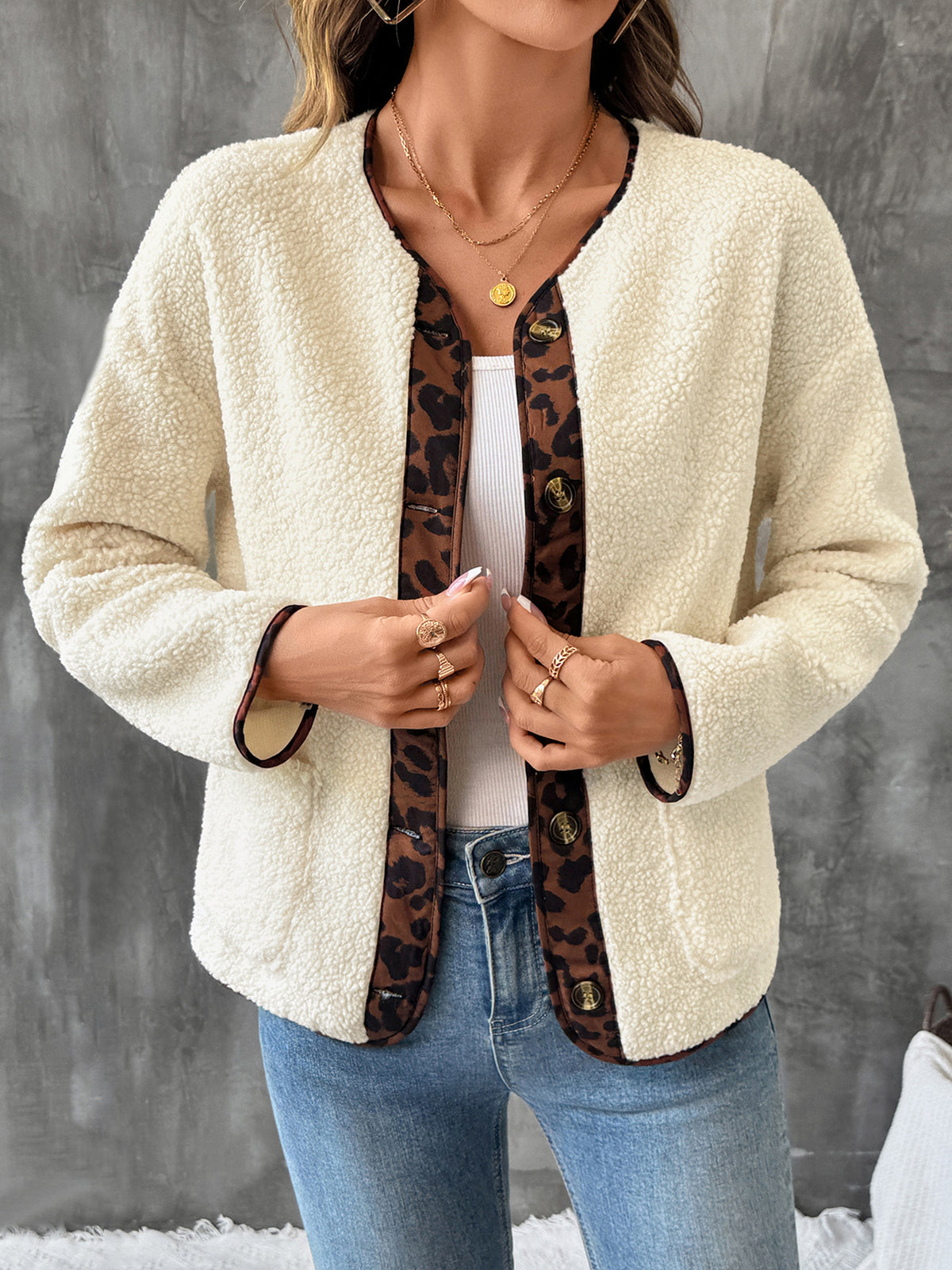 Person wearing a cream sherpa jacket with leopard print trim against a gray background