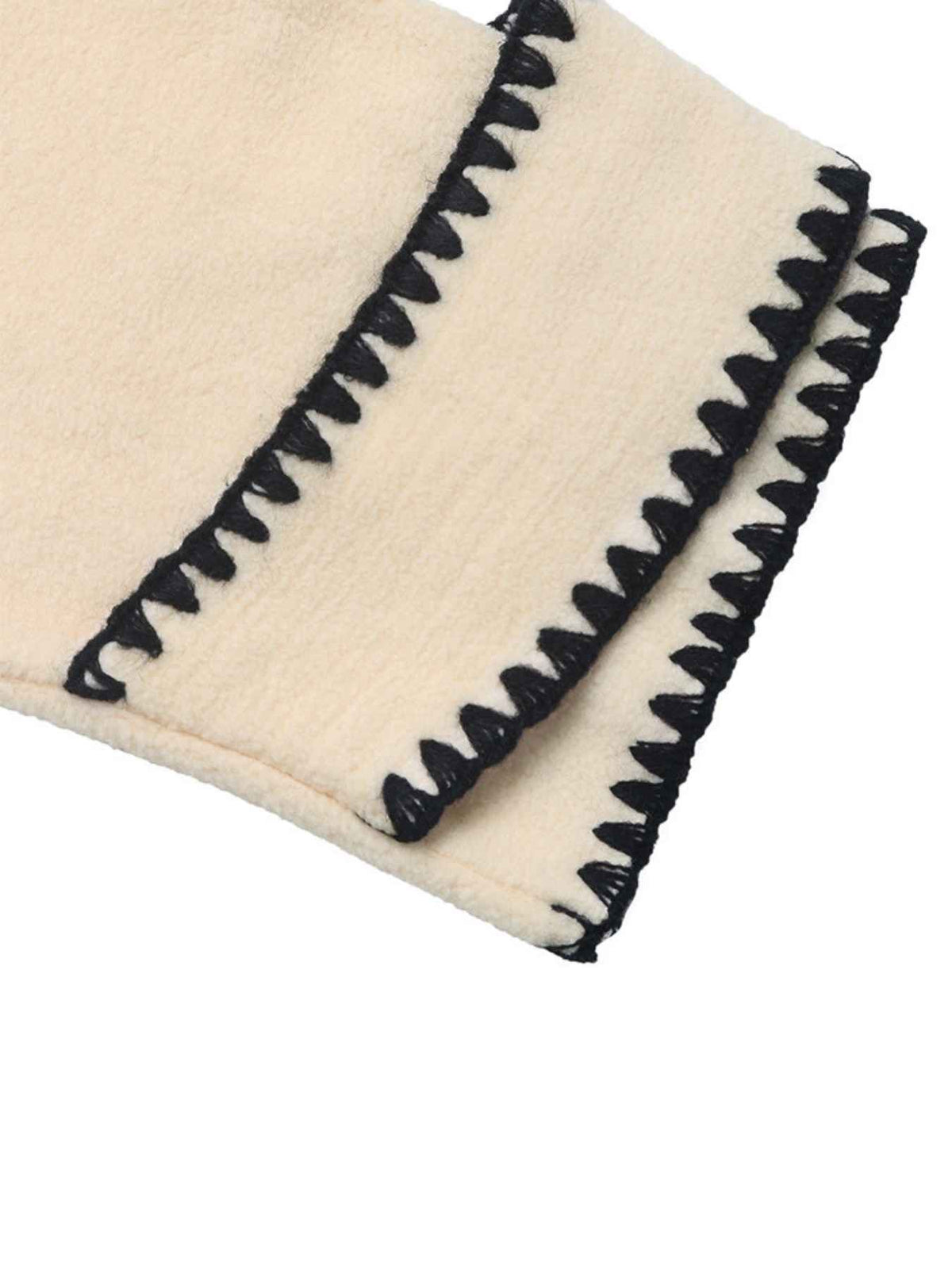 A close-up of a cream-colored textured fabric item, likely a blanket or throw, featuring a black zigzag stitched border.