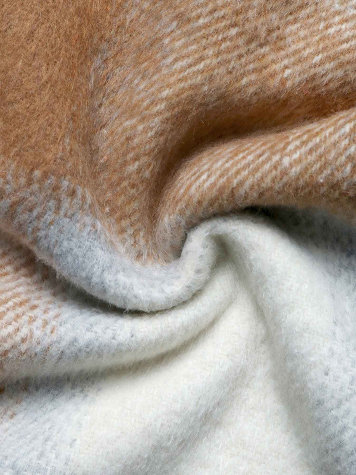 A close-up of soft woven fabric with a warm tan and cream plaid pattern, draped to show texture and color variation.